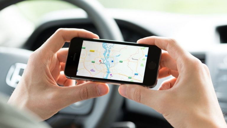 Záber na ruky človeka, v ktorých drží smartfón a v ňom má vyobrazenú mapu od Google (je v aute). Zdroj: iStockphoto.com