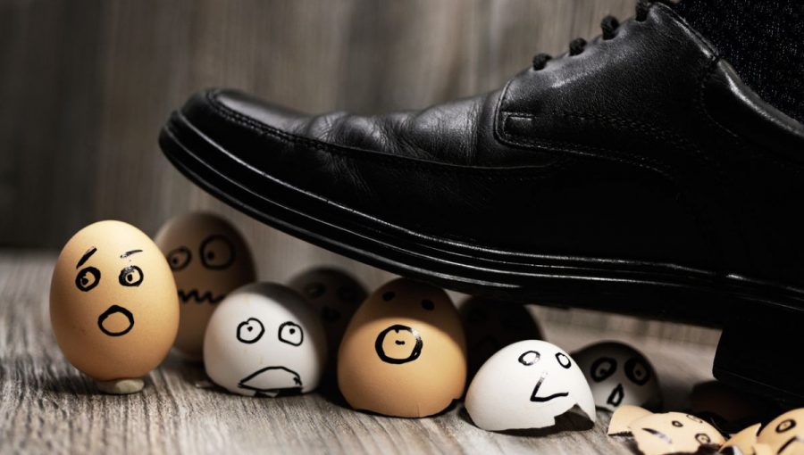 Noha muža v čiernej topánke šliape po vajíčkach, na ktorýách sú namaľované vydesené tváre. Obrázok ilustruje moc a strach. Zdroj: iStockphoto.com