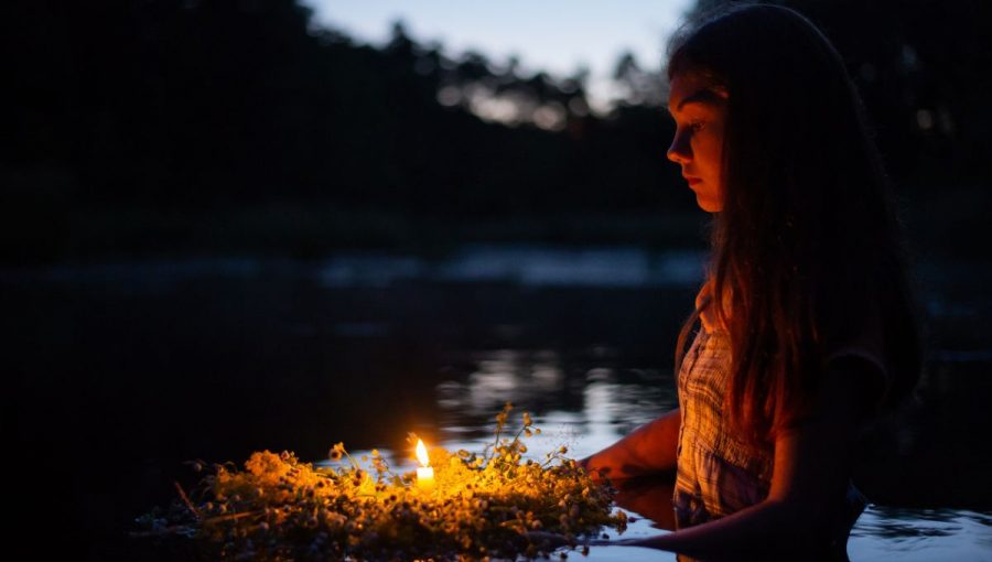 Dievča drží uvitý veniec, v ktorom je zapálená sviečka.