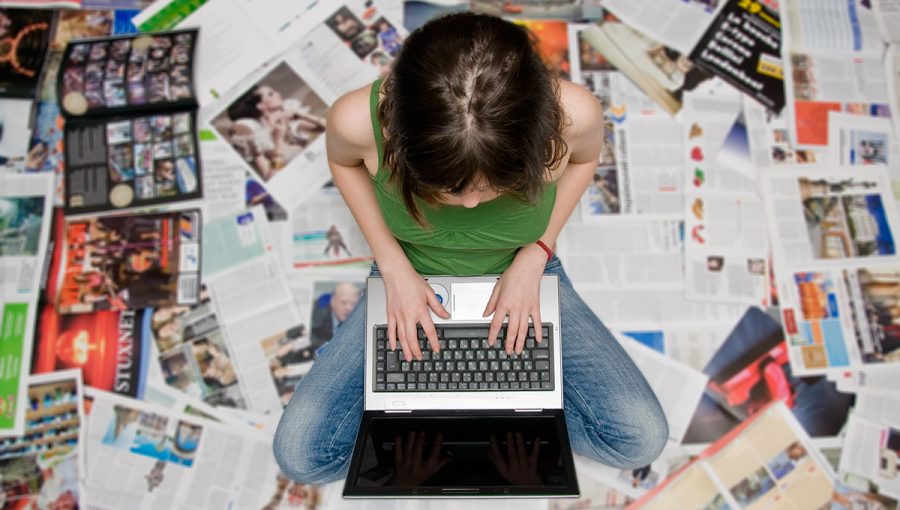 Tínedžerka s laptopom sediaca na novinách. Zdroj: iStockphoto.com