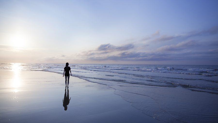 Žena sa prechádza po pláži pri východe slnka. Zdroj: iStockphoto.com