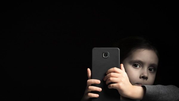 Malé dieťa vykúka spoza veľkého smartfónu
