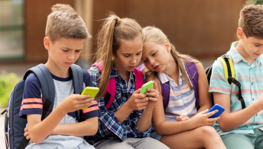skupinka deti so skolskymi taskami pozera do mobilnych telefonov