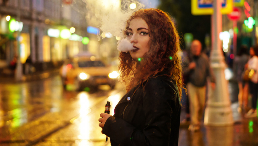 Mladá červenovlasá žena fajčí e-cigaretu