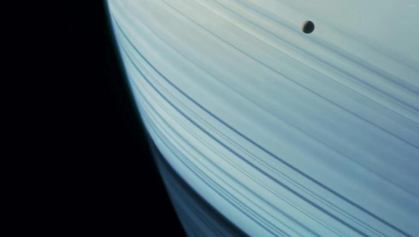 Saturn pruhovaný tieňmi svojich prstencov sa vynára za svojim mesiacom Mimas. Zdroj: NASA