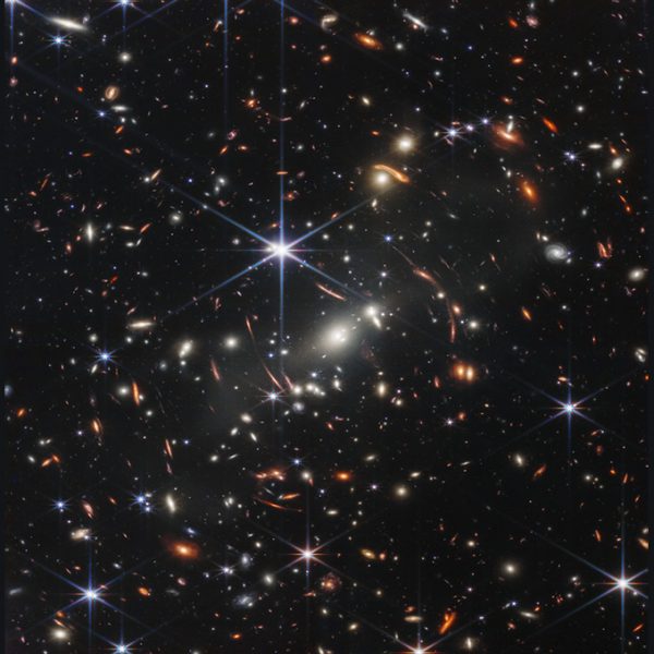 Na infračervenej snímke z JWST sú tisíce galaxií v kope galaxií SMACS 0723. Jasná biela galaxia v strede pôsobí ako gravitačná šošovka, ktorá umožňuje pozorovať aj vzdialenejšie galaxie. Tie majú pretiahnutý tvar a podľa vedcov ide o prevažujúci tvar galaxií v ranom vesmíre. Zdroj: NASA