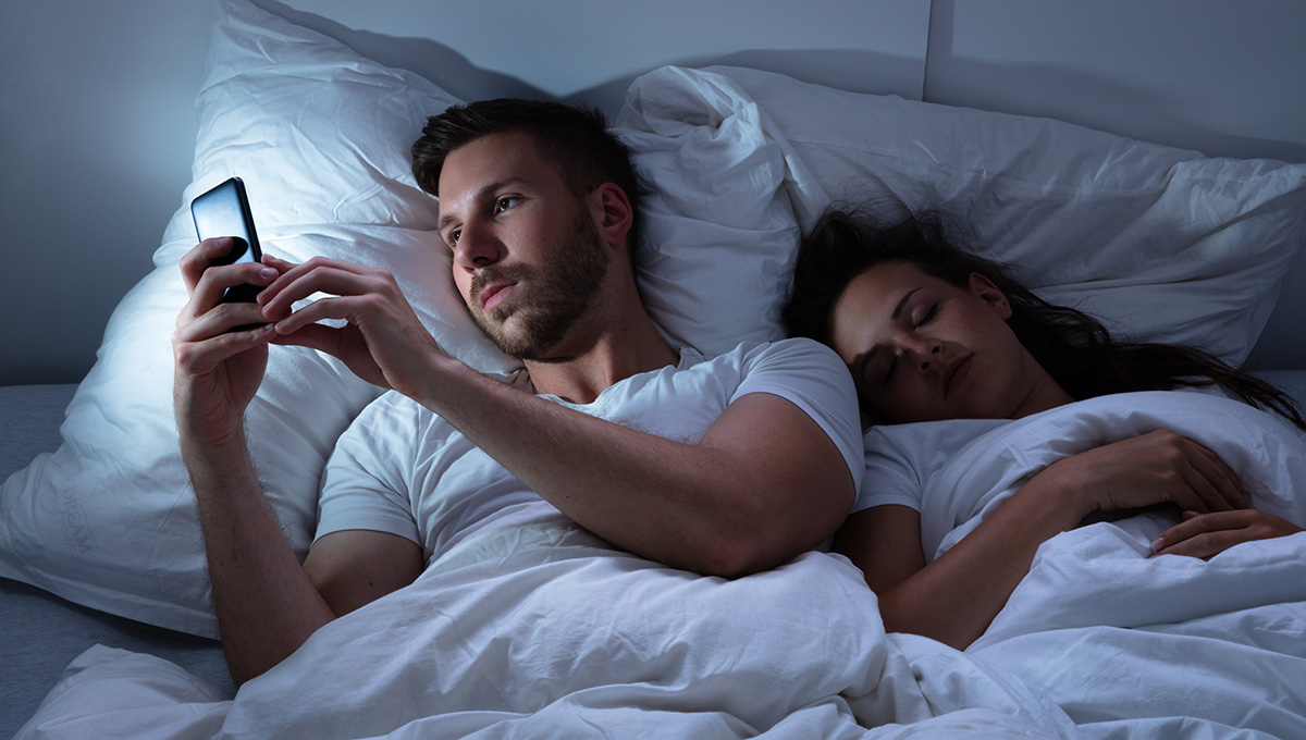 Muž chatuje v noci pri spiacej žene. Zdroj: iStock.com/AndreyPopov
