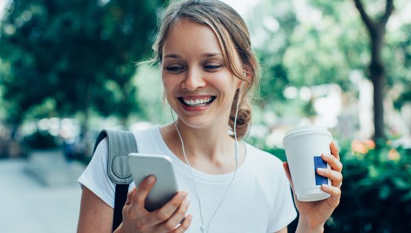 Žena s mobilom a kávou v ruke. Zdroj: iStock.com/MangoStar_Studio
