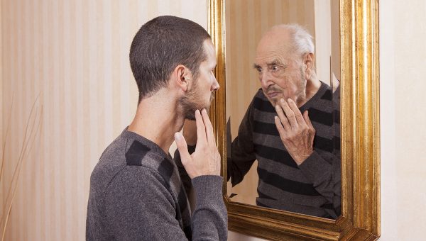 Mladý muž vidí sám seba v zrkadle ako starého. Zdroj: iStock.com/tommasolizzul