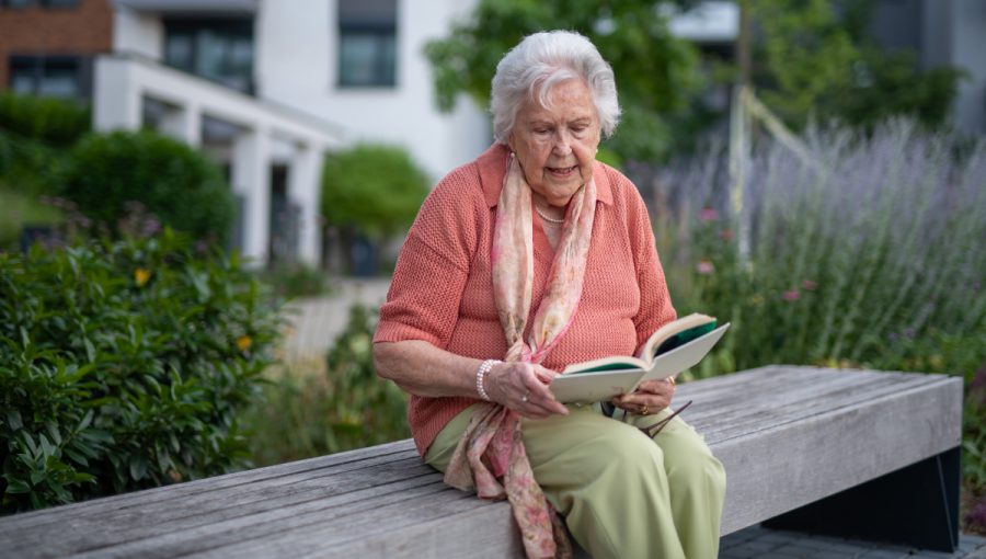 Seniorka číta knihu v parku. Zdroj: iStock.com/Halfpoint