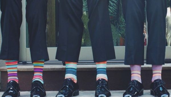 Tri páry mužských nôh v čiernych lakovkách a farebných pruhovaných ponožkách. Zdroj: Pexels.com