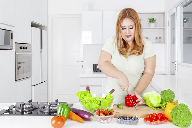 Ilustračné foto. Žena s nadváhou krája zeleninu v kuchyni. Zdroj: iStock