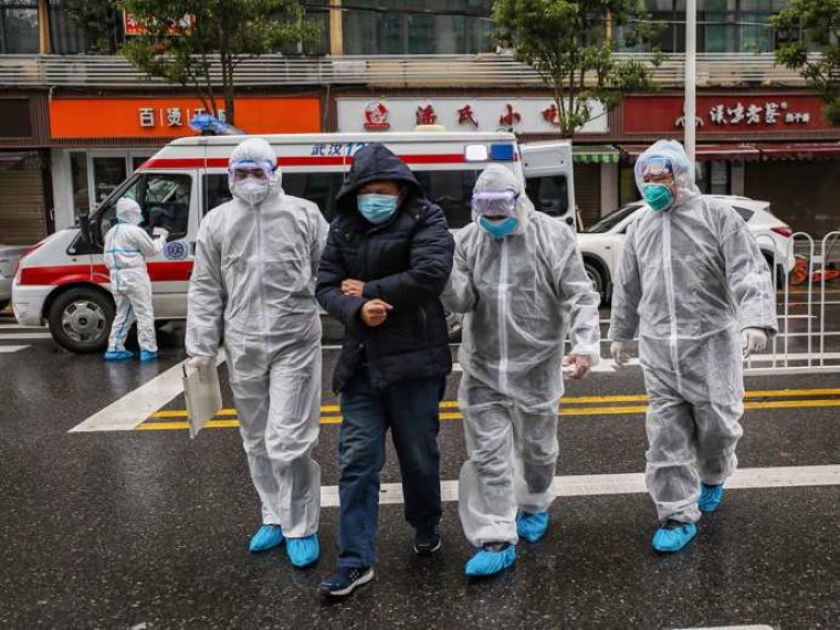 Na foto z dnešných dní traja čínsky zdravotníci v ochranných oblekoch pridŕžajú chorého pacienta. Zdroj: GETTY IMAGES 